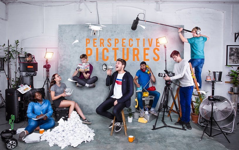 A group of young people striking poses in a studio with the words 'Perspective Pictures' overlaid on the backdrop. Rupert Rixon sits in the middle holding a megaphone.